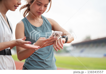 Close up of asian woman friends checking time on phone and watch while exercising in sports stadium. 138343557