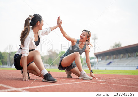 Asian woman clapping hand high five a friend as sitting crouching on running track in sports stadium Asian woman clapping hand high five a friend as sitting crouching on running track in sports stadium 138343558