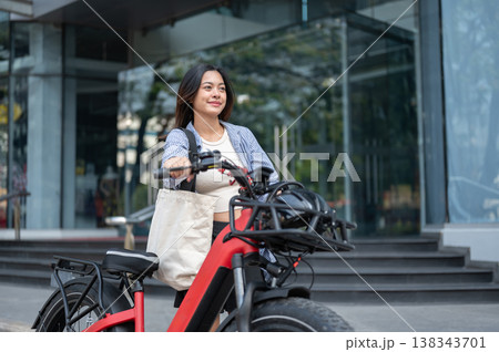 Pretty asian woman walking with a fat tire electric bicycle in front of a shopping mall or building. 138343701