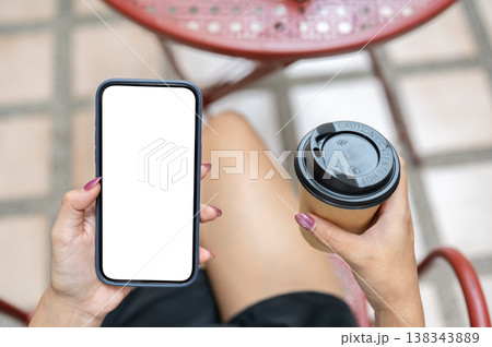 Top view of woman's hand holding white screen phone with coffee cup sitting at table in outdoor cafe Top view of woman's hand holding white screen phone with coffee cup sitting at table in outdoor cafe 138343889