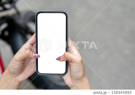 Top view of a woman's hands holding white screen smartphone standing on street pavement with bicycle Top view of a woman's hands holding white screen smartphone standing on street pavement with bicycle 138343893