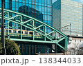 都会のビル群に架かる鉄橋と通勤電車 138344033