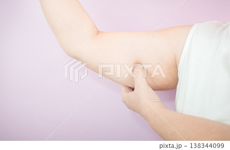 Caucasian overweight woman pinching arm fat while flexing muscle 138344099