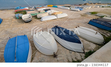 Colorful rowboats and dinghies resting upside down on rocky waterfront under soft daylight, creating quiet seaside harbor mood Colorful rowboats and dinghies resting upside down on rocky waterfront under soft daylight, creating quiet seaside harbor mood 138344117