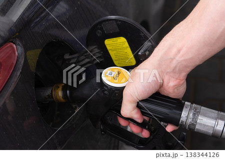 Close up of hand holding diesel pump nozzle inserted into car fuel tank, showing refueling process and transport theme Close up of hand holding diesel pump nozzle inserted into car fuel tank, showing refueling process and transport theme 138344126