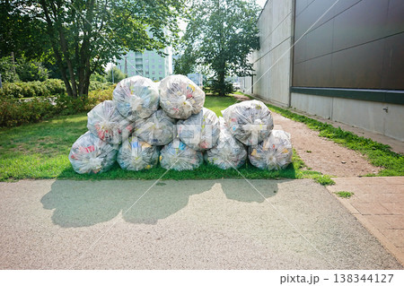 Clear bags packed with plastic bottles stacked outdoors near path and buildings, showing deposit return collection and recycling effort Clear bags packed with plastic bottles stacked outdoors near path and buildings, showing deposit return collection and recycling effort 138344127