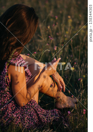 Beautiful girl in hat sitting on a flower meadow at sunset Beautiful girl in hat sitting on a flower meadow at sunset 138344303