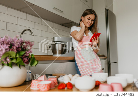 Young woman planning to cook, looking for recipe on internet on her smartphone at home kitchen Young woman planning to cook, looking for recipe on internet on her smartphone at home kitchen 138344482