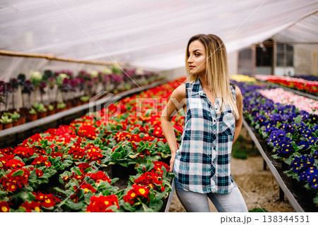 Women gardener in botanic garden,planting flowers and decorate.Smiling happy girl work in the garden.Young woman with scarf and cap kneeling between blooming plants. Women gardener in botanic garden,planting flowers and decorate.Smiling happy girl work in the garden.Young woman with scarf and cap kneeling between blooming plants. 138344531