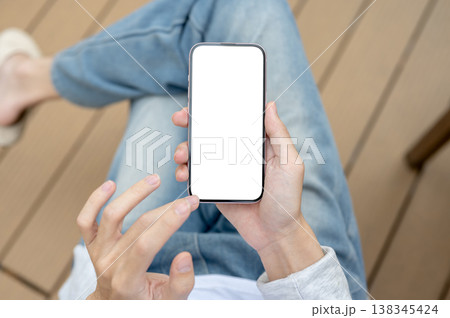 Top view of a man's hands holding using white screen phone while sitting on chair over wooden floor. 138345424