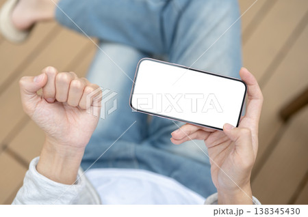 Top view of man's hand holding white screen phone horizontally making a fist while sitting on chair. 138345430
