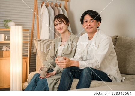 家のリビングのソファーで談笑する若いアジア人夫婦,カップル 138345564