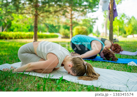 Flexible women in beige and green activewear stretching in childs pose on mat outdoors in city park. Childs pose, stretching, mat, outdoor, women, park. Flexible women in beige and green activewear stretching in childs pose on mat outdoors in city park. Childs pose, stretching, mat, outdoor, women, park. 138345574