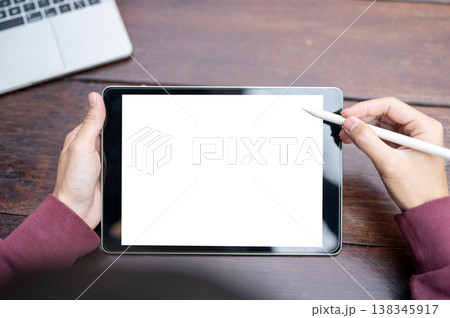 Top view of a man's hand holding a stylus pen over white screen tablet while sitting at wooden table 138345917