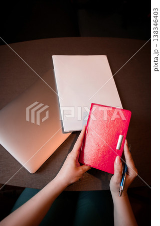 Close-up of female hands holding a red notebook and pen. Close-up of female hands holding a red notebook and pen. 138346403