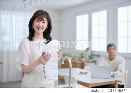 キッチンでお皿を拭きながら笑顔で話す60代女性と男性 138346874