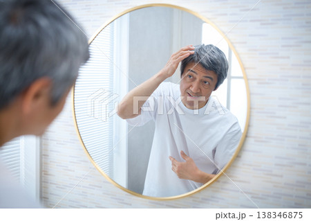 鏡を見て白髪を気にする60代の男性 138346875