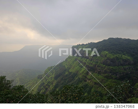 Wide view of green hills and valleys under cloudy skies in Matheran, capturing a serene monsoon atmosphere in the Western Ghats. Wide view of green hills and valleys under cloudy skies in Matheran, capturing a serene monsoon atmosphere in the Western Ghats. 138347068