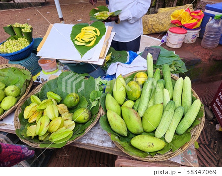 Indian roadside fruit stall displaying fresh amla, guava, groundnuts, cucumbers, and sliced mango served on leaves, reflecting local street food culture. 138347069
