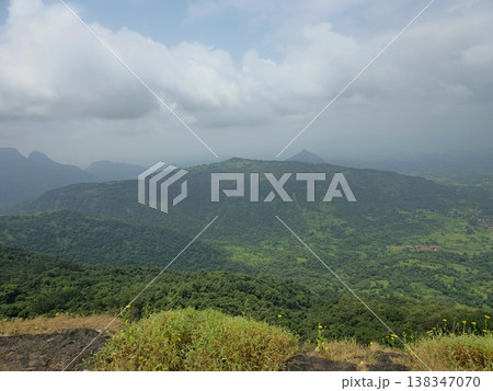 Wide view of lush green hills and valleys under cloudy skies, showcasing the scenic landscape and natural beauty of Matheran hill station. 138347070