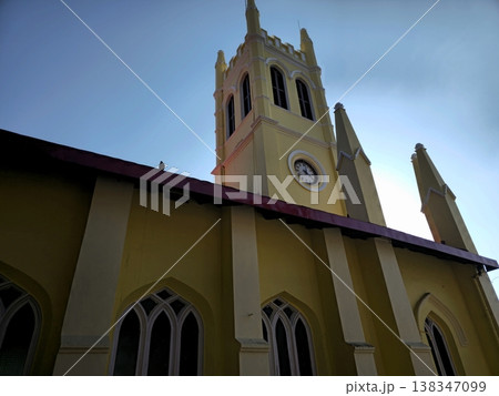 Low-angle view of Christ Church Shimla showing its tall clock tower and yellow facade against a clear sky, highlighting colonial-era architecture and historic charm. 138347099