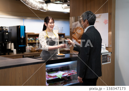 笑顔で接客をして注文の品を渡すカフェの女性店員 138347173