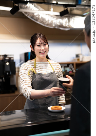 笑顔で接客をして注文の品を渡すカフェの女性店員 138347175