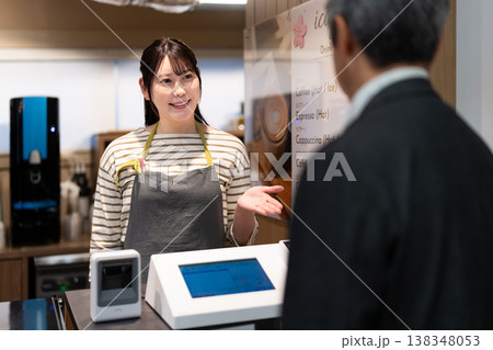 レジで電子マネーでの支払いを案内する笑顔のカフェ店員 レジで電子マネーでの支払いを案内する笑顔のカフェ店員 138348053