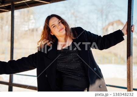 Portrait of smiling slavic woman with light brown hair wearing black coat and elegant outfit posing playfully with outstretched arms in soft sunlight Portrait of smiling slavic woman with light brown hair wearing black coat and elegant outfit posing playfully with outstretched arms in soft sunlight 138348232