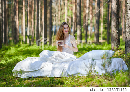 Young woman has breakfast in bed in a summer forest Young woman has breakfast in bed in a summer forest 138351153