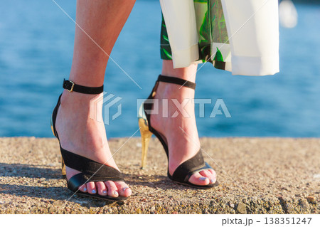 Woman feet in high heels shoes on sea pier Woman feet in high heels shoes on sea pier 138351247
