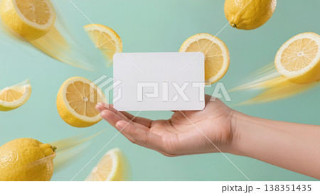Fresh lemons float around a blank card held in hand in kitchen, cafe, or nature setting. Suitable for banners, advertising, menus, articles, and web design. 138351435