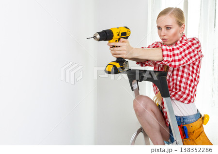 Woman using drill on ladder Woman using drill on ladder 138352286