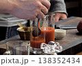 Pouring tomato juice into glasses through spoon. 138352434