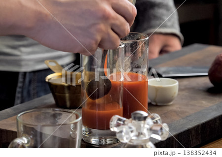 Pouring tomato juice into glasses through spoon. Pouring tomato juice into glasses through spoon. 138352434