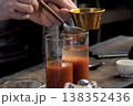 Pouring tomato juice into glasses through spoon. 138352436