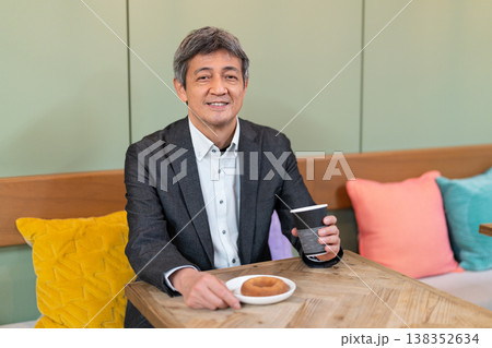 カフェでコーヒーとドーナツを手に笑顔で休憩するシニアビジネスマン カフェでコーヒーとドーナツを手に笑顔で休憩するシニアビジネスマン 138352634