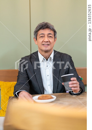 カフェでコーヒーとドーナツを手に笑顔で休憩するシニアビジネスマン 138352635