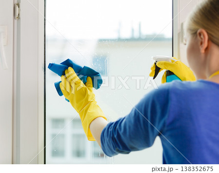 Girl cleaning window at home using detergent rag Girl cleaning window at home using detergent rag 138352675