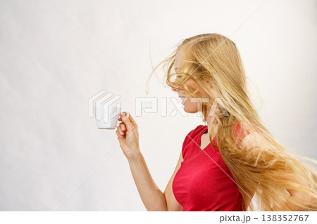Blonde girl blowing hair holds coffee cup 138352767