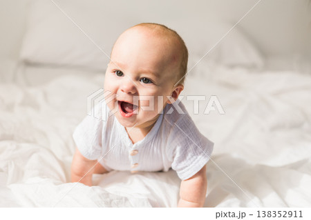 Smiling happy newborn baby on a white bed at home, the concept of a happy healthy infant baby. Generation alpha and gen alpha Smiling happy newborn baby on a white bed at home, the concept of a happy healthy infant baby. Generation alpha and gen alpha 138352911