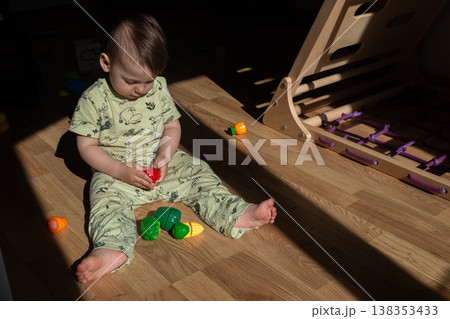 Toddler playing with toy vegetables on sunlit wooden floor Toddler playing with toy vegetables on sunlit wooden floor 138353433
