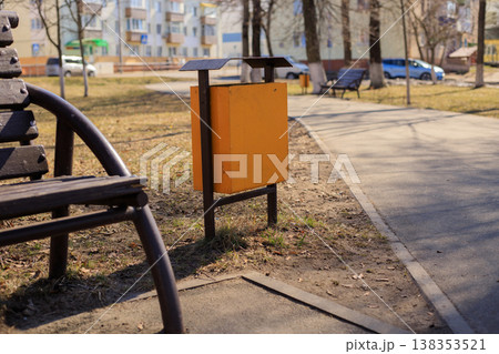 Yellow metal trash can in a public city park near a walking path. Yellow metal trash can in a public city park near a walking path. 138353521