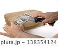 Cutting US dollar banknotes on a wooden chopping board with a knife 138354124