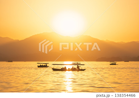 Golden sunset over West Lake with traditional boats carrying passengers in Hangzhou, China Golden sunset over West Lake with traditional boats carrying passengers in Hangzhou, China 138354466