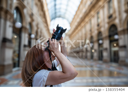 Middle aged woman visiting milan, italy, actively capturing architectural details and the iconic glass roof of galleria vittorio emanuele ii with a digital camera, engaged in travel photography 138355404