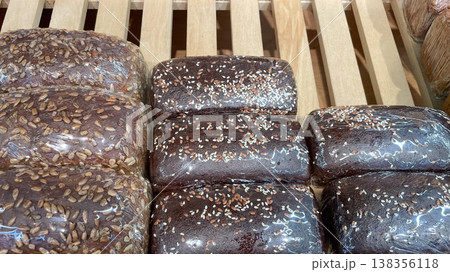 Assorted dark rye and whole grain bread loaves topped with seeds in retail packaging on wooden rack 138356118