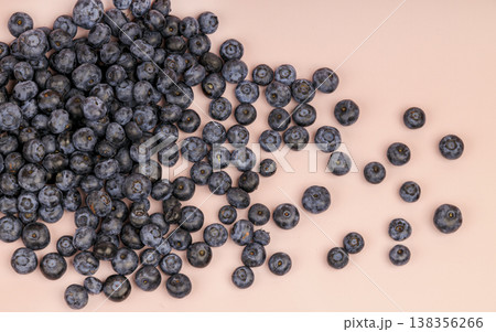 High angle view of organic blueberries spread across a soft pink surface. The image captures the natural texture and waxy bloom of the fresh fruit High angle view of organic blueberries spread across a soft pink surface. The image captures the natural texture and waxy bloom of the fresh fruit 138356266