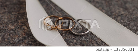 Banner Wedding rings on white ribbon on dark stone surface Banner Wedding rings on white ribbon on dark stone surface 138356331