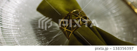 Banner Green cloth napkin with gold ring on white glass plate on dark background 138356397